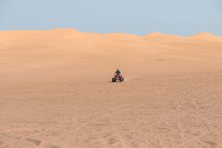 Man riding quadbike in desert against clear sky