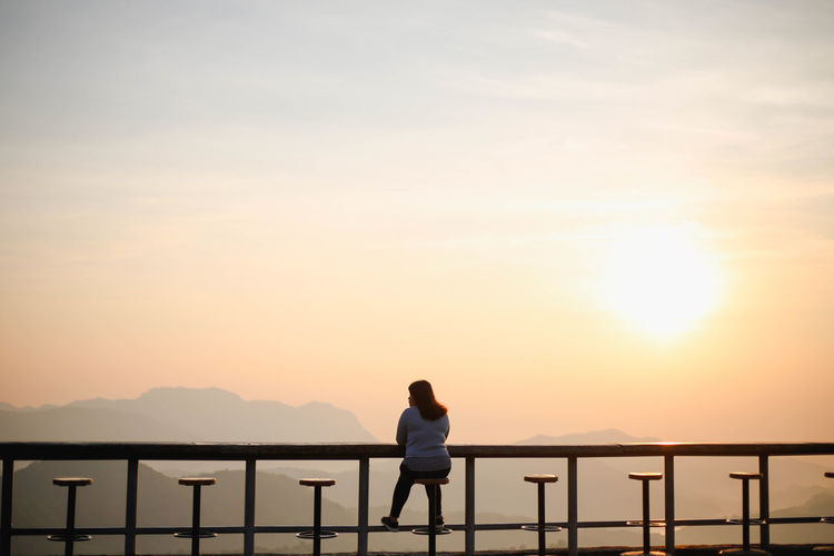 Woman sitting on seat against sky during sunset
