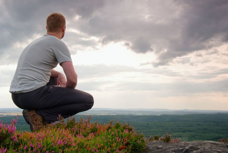Hiker in squatting position on a rock in heather bushes, enjoy the scenery