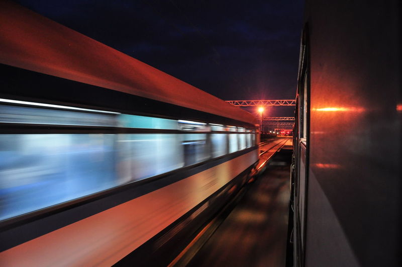 Blurred motion of train at illuminated railroad station against sky