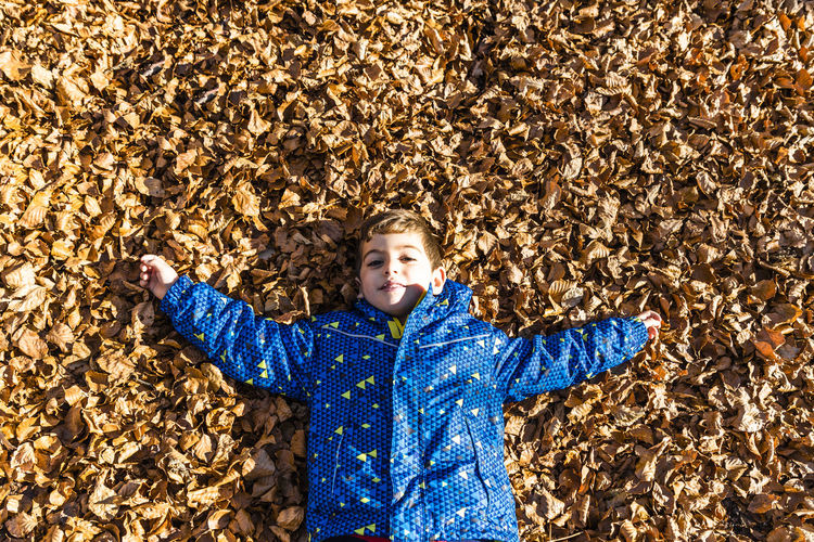 High angle portrait of boy lying on dry leaves during autumn