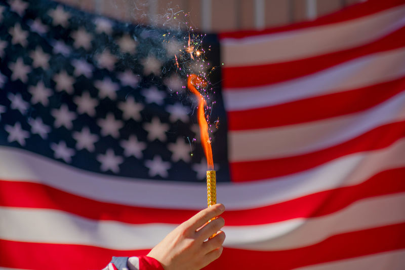 Close-up of hand holding firework against american flag