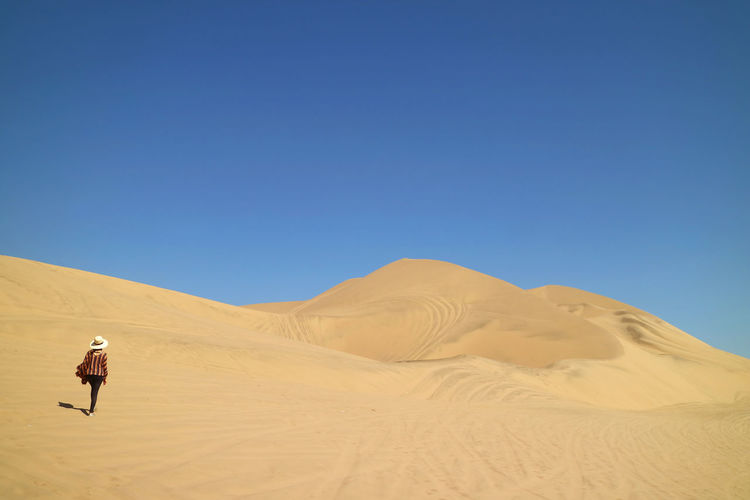 Rear view of woman walking on sand at desert against sky