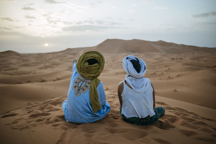 People sitting on sand dune in desert against sky