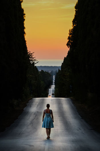 Rear view of woman standing on road against sky during sunset