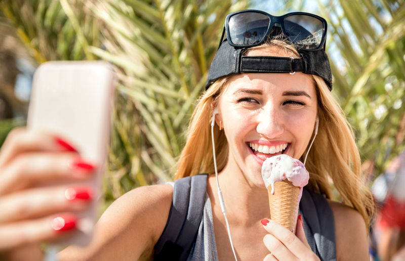 Smiling young woman taking selfie while eating ice cream