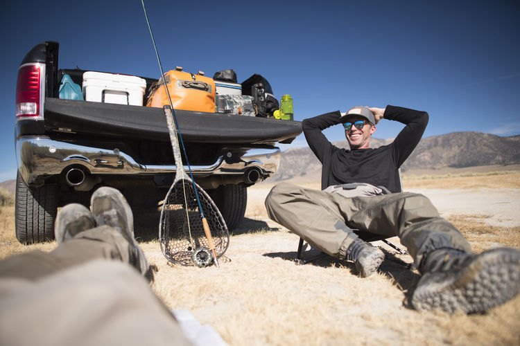 A fly fisherman's relaxes by his tailgate after a day of fishing.