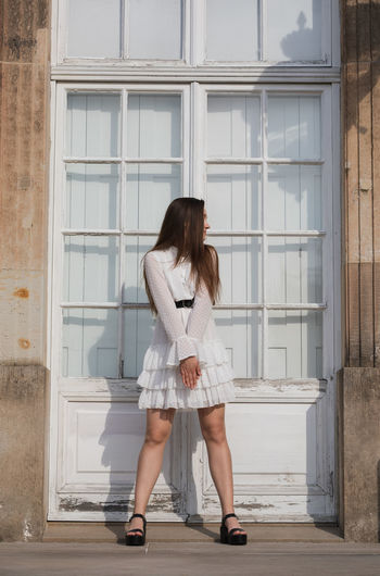 Full length of young woman standing against white door