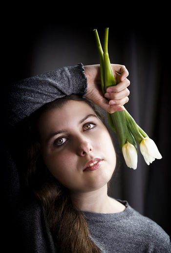 Portrait of beautiful young woman holding flowers against black background