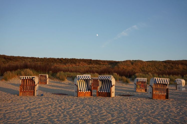 Hooded beach chairs on sand against blue sky during sunset
