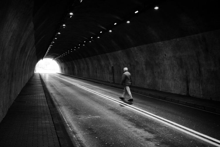 Rear view of man walking on illuminated tunnel