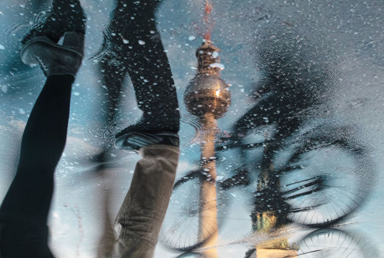 Reflection of  bicycle and pedestrians in puddle, television tower as background