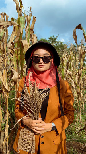 Portrait of young woman wearing sunglasses while standing on field against sky