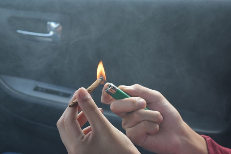 Cropped hands burning marijuana joint in car