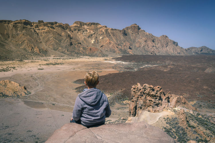 Rear view of boy sitting on rock at desert