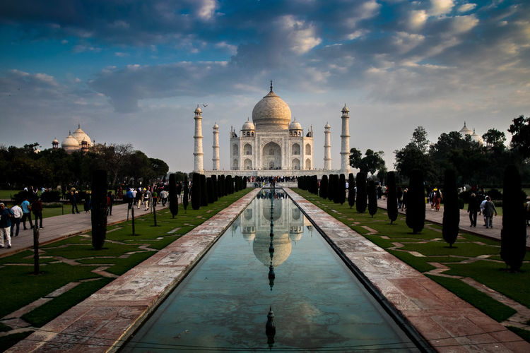 Reflection of taj mahal on reflecting pool against cloudy sky