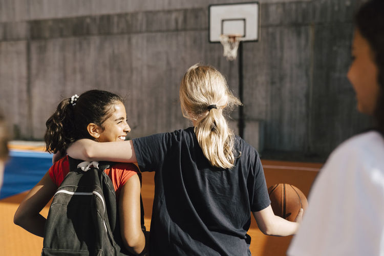 Blond girl with arm around female friend while walking in basketball court