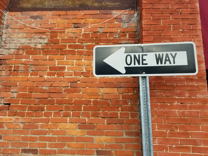 Low angle view of one way sign on brick wall