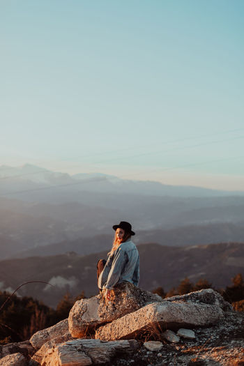 Young woman sitting against mountains on rock during sunset