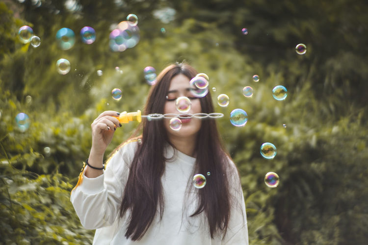 Young woman blowing bubbles against trees