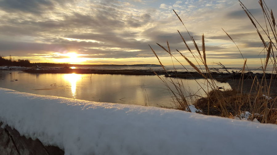Snow covered retaining wall by lake against sky during sunset