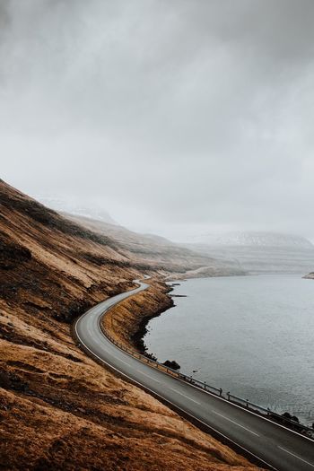 Scenic view of road by lake against sky during foggy weather