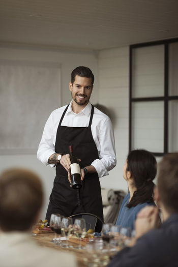 Happy man showing wine bottle to business people at table