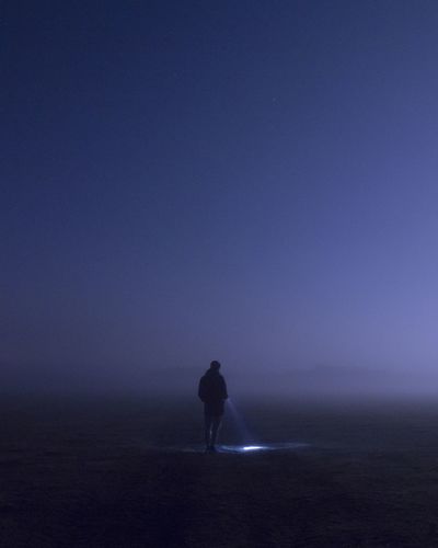 Rear view of silhouette man standing on field against sky at night