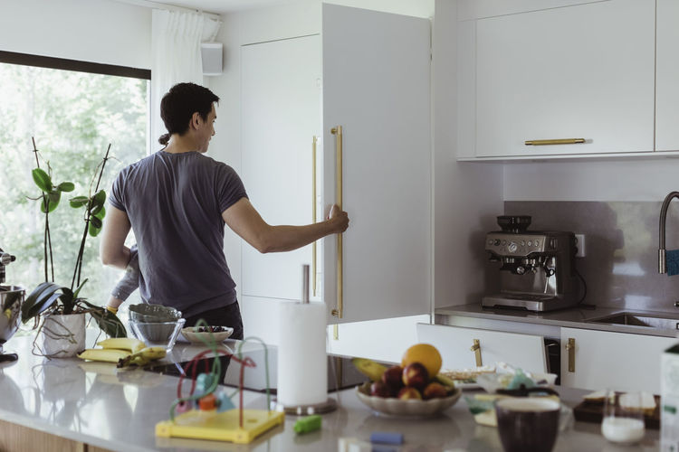 Father opening refrigerator while carrying baby son in kitchen