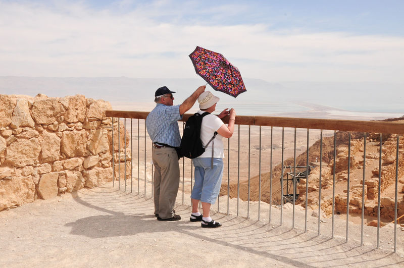 Senior man and woman standing with umbrella on beach 