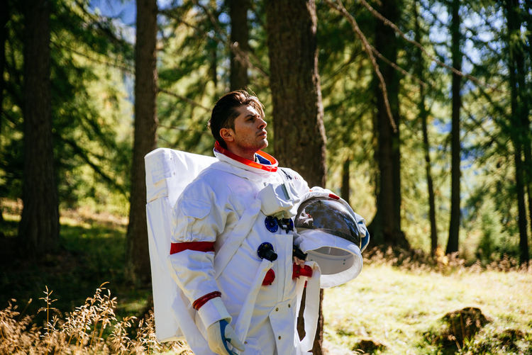Astronaut looking away while standing in forest
