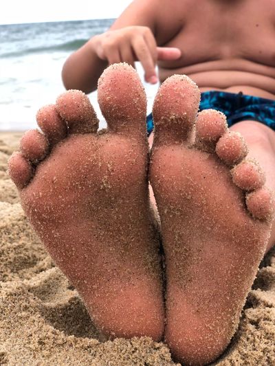 Close-up of messy feet of man sitting on sand at beach