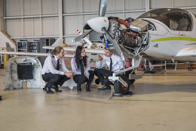 Engineer showing airplane wheel to trainees while crouching on floor in hangar