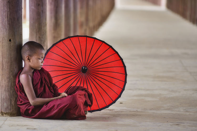 Monk with red umbrella sitting in temple