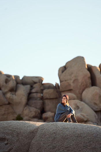 Woman sitting on rock against clear sky