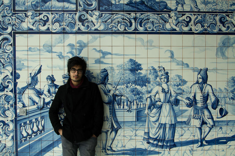 Portrait of young man standing against blue painted tiled wall