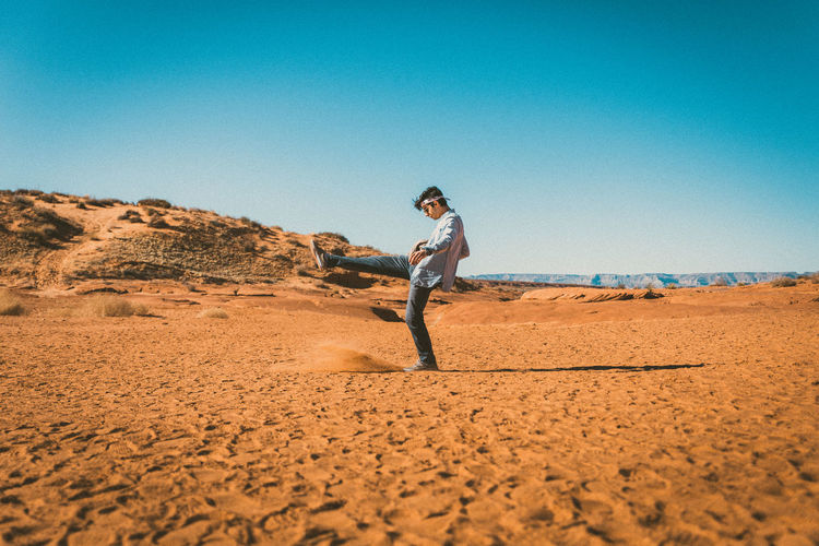 Side view of man kicking sand in desert