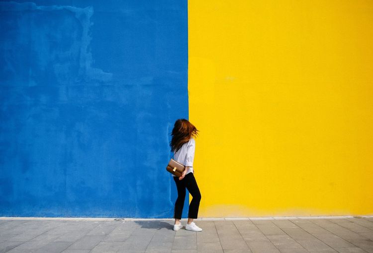 Full length of young woman against yellow wall