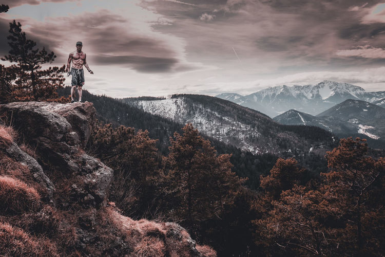 Shirtless man standing on mountain against sky