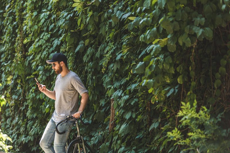 Young man using mobile phone while standing on tree