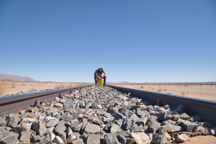 Man sitting on railroad track against blue sky