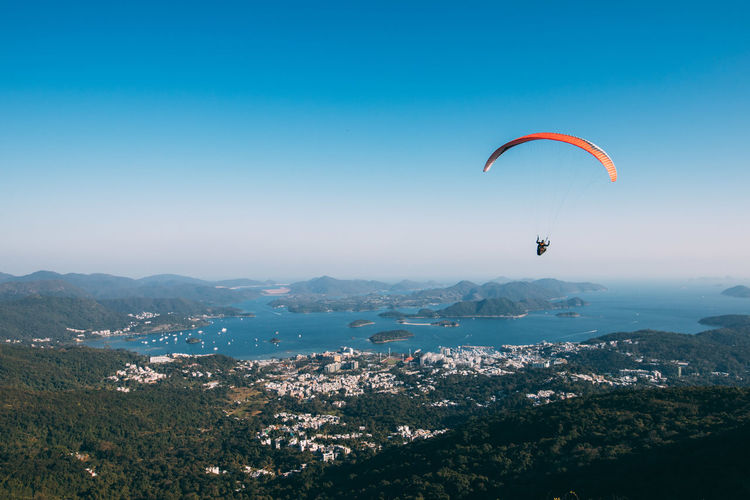 Person paragliding over cityscape against sky