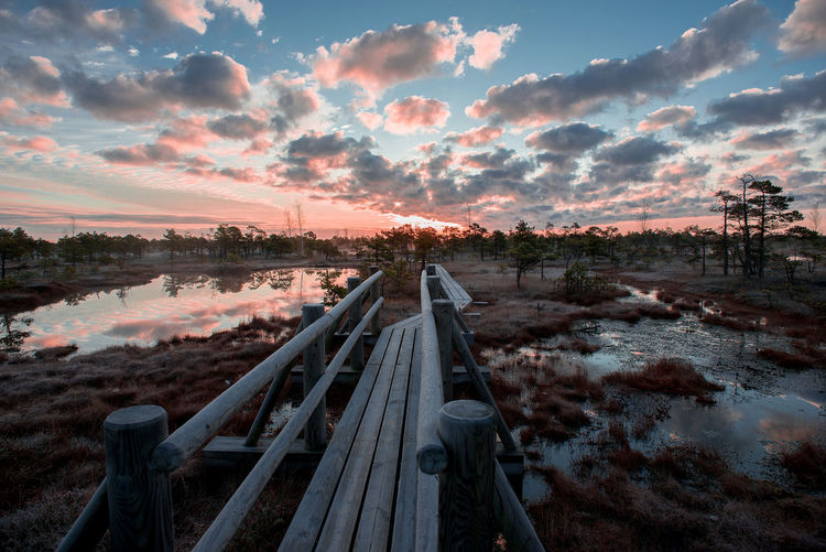 Footbridge on wetland against sky during sunset