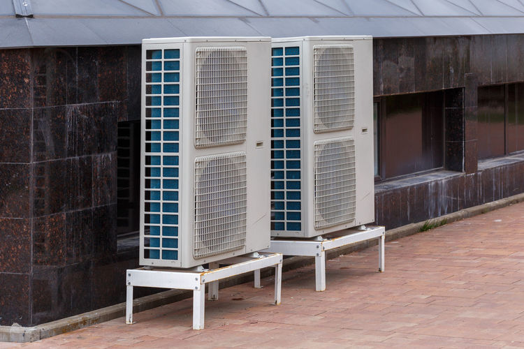 Two double condensing units of air conditioner on the ground level near granite building wall