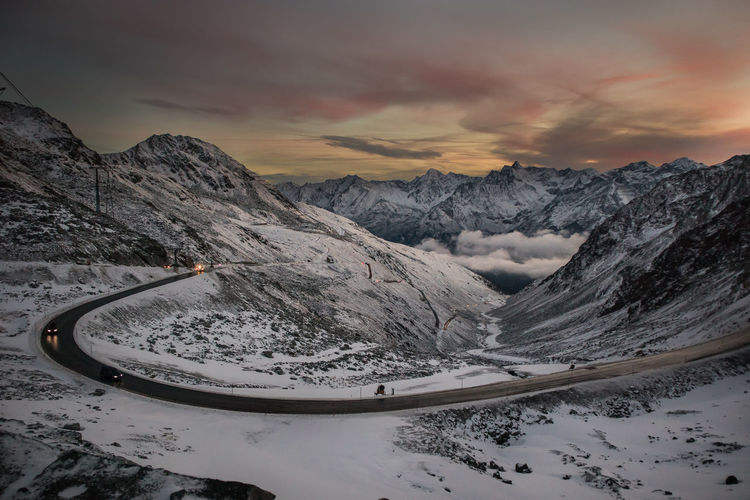 Road by snowcapped mountains against sky during sunset