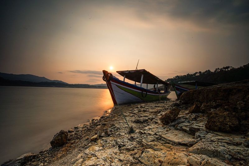 Boat moored on sea against sky during sunset