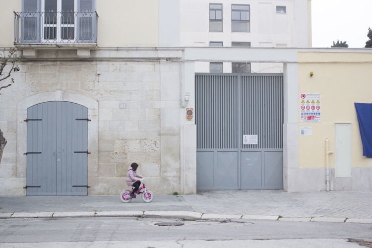 Girl riding bicycle on footpath by building