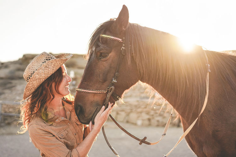 Woman standing by horse during sunset