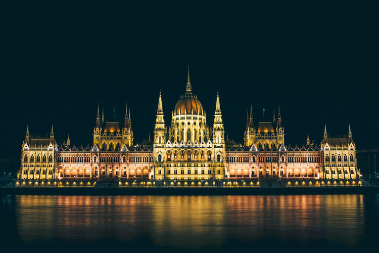 Illuminated hungarian parliament building by river against clear sky at night