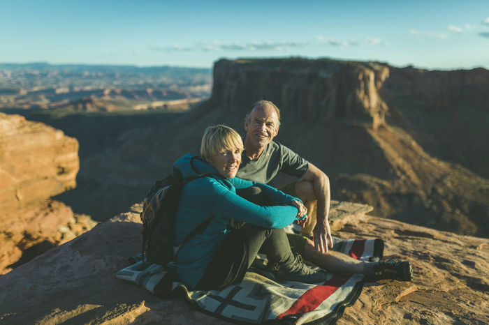 Portrait of hiking couple sitting on mountain against rock formation at canyonlands national park